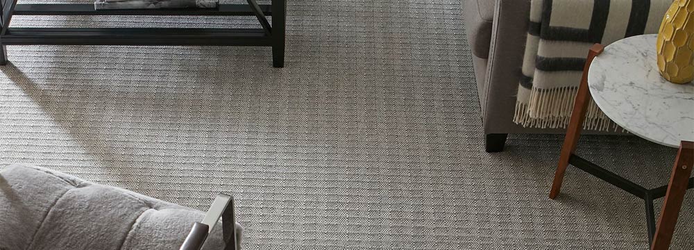 Tan patterned carpet with light blue couch and brown chair